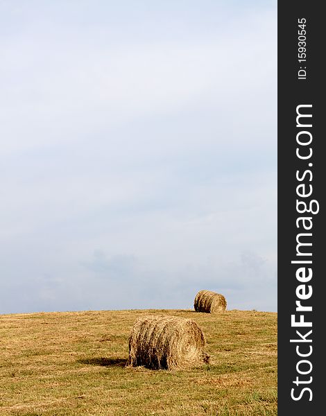 Two bales of hay lay on a field. Plenty of sky for copy-space. Two bales of hay lay on a field. Plenty of sky for copy-space.