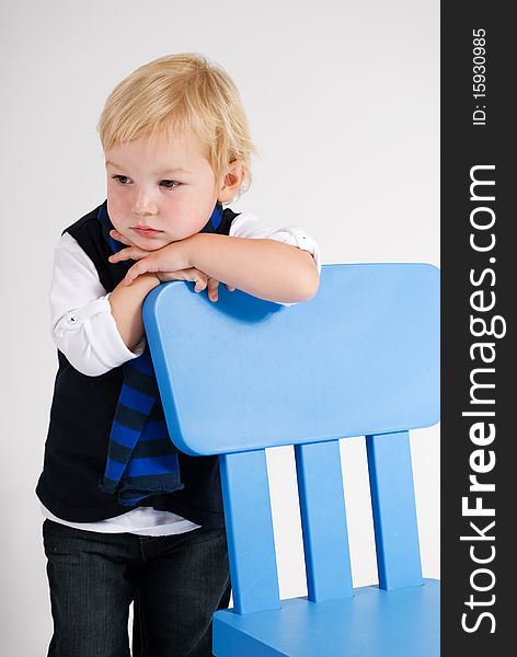 A vertical image of a handsome young blonde boy leaning on a blue chair deep in thought. A vertical image of a handsome young blonde boy leaning on a blue chair deep in thought