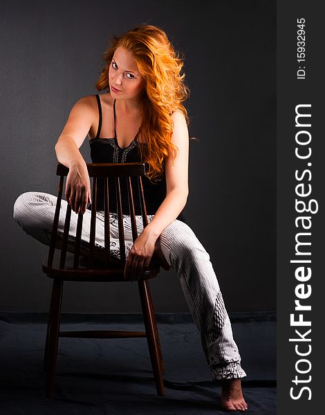 Portrait of a beautiful redheaded woman in a chair on a dark background. Portrait of a beautiful redheaded woman in a chair on a dark background