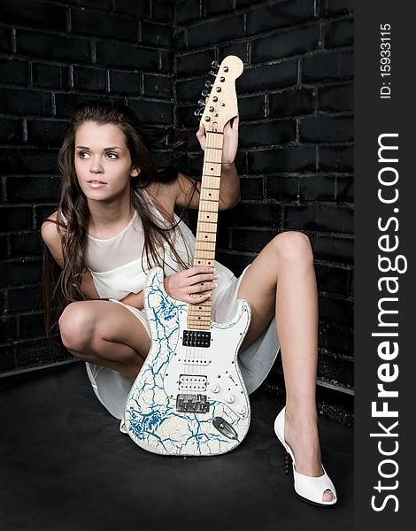 The woman with a white guitar against a black wall