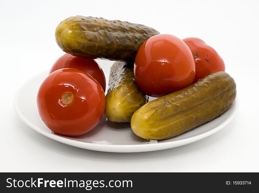 Homemade salted tomatos and cucumber on a plate on a white background. Homemade salted tomatos and cucumber on a plate on a white background