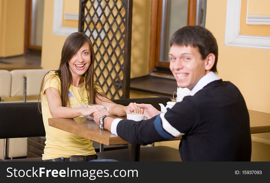 Young and positive smiling pair sit in cafe