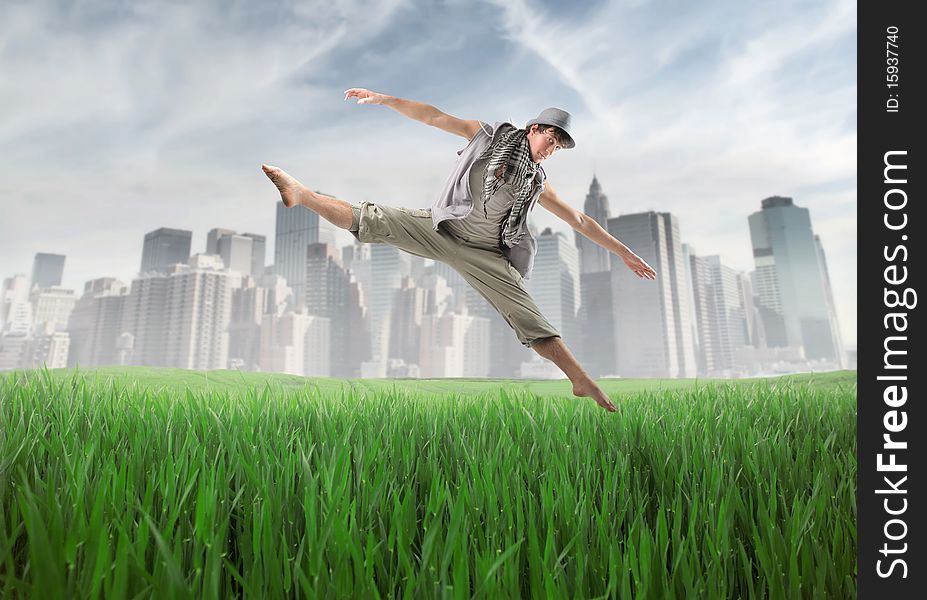 Young man dancing and jumping on a green meadow with cityscape on the background. Young man dancing and jumping on a green meadow with cityscape on the background