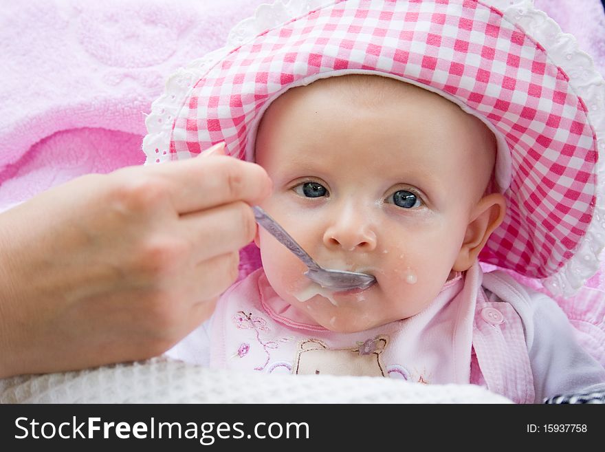 Little girl sits in a carriage and she is fed from a spoon. Little girl sits in a carriage and she is fed from a spoon