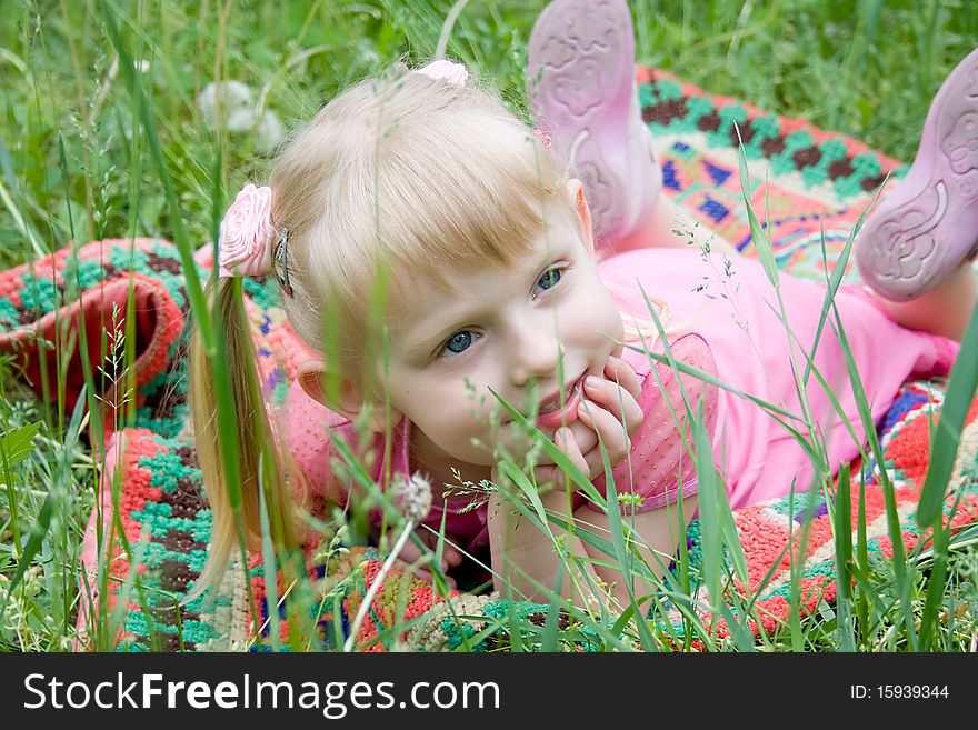 Little girl lies on a carpet on a grass smiles. Little girl lies on a carpet on a grass smiles