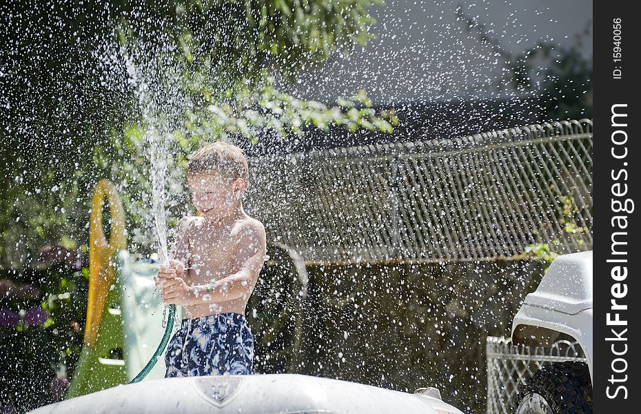 Young boy playing with a hose pipe in the Garden on a sunny day. Young boy playing with a hose pipe in the Garden on a sunny day