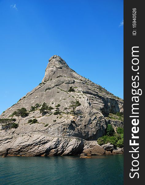 Steep high rock between the blue sky and emerald sea. Steep high rock between the blue sky and emerald sea.