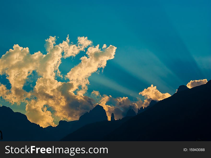 Rays of sun peeking out from behind a mountain, creating cuts in the sky at sunset. Rays of sun peeking out from behind a mountain, creating cuts in the sky at sunset