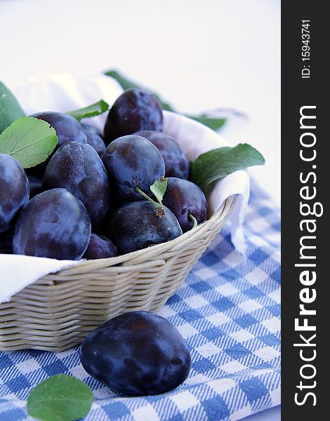 Many plums in a basket on a blue napkin