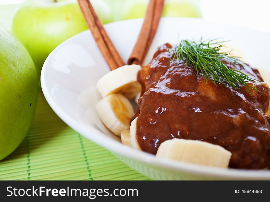 Bananas with chocolate and cinnamon and green apples on background.