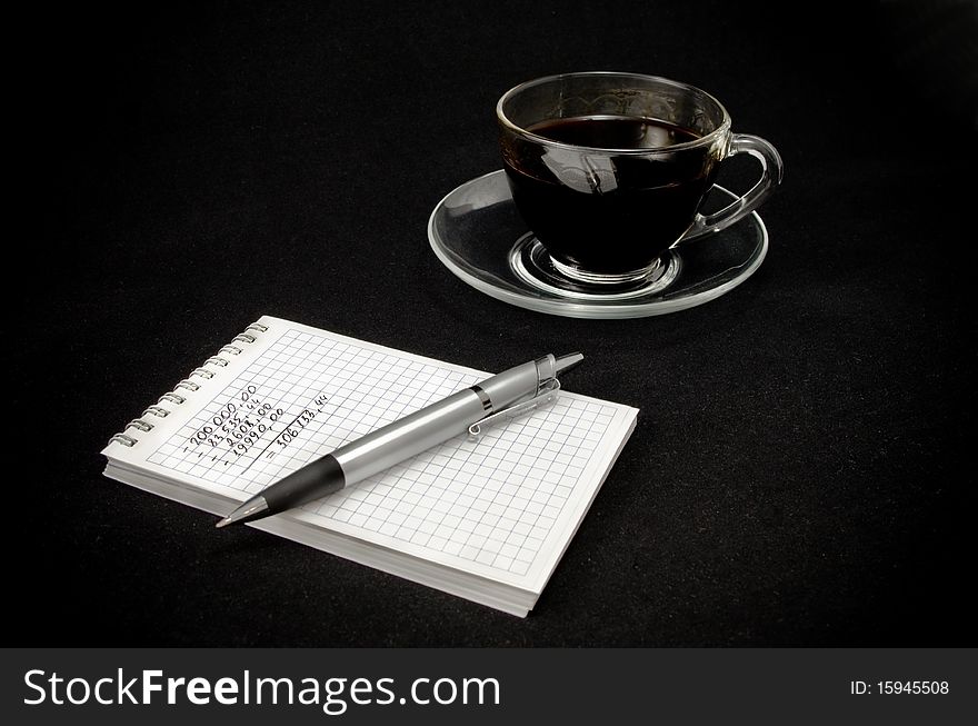 Cup of coffee and a notepad with a pen on a dark b