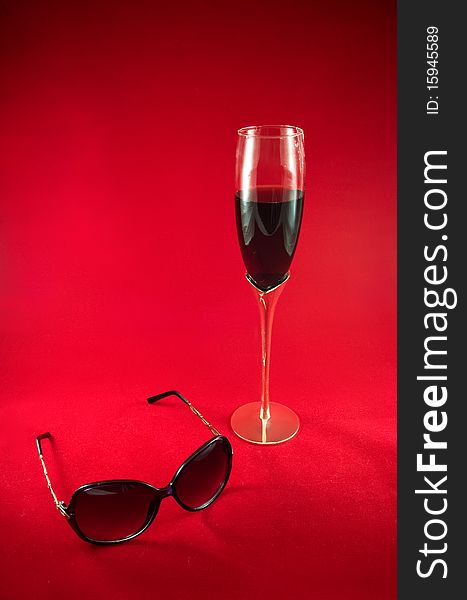 Wineglass with red dry wine and sunglasses on a red background. Wineglass with red dry wine and sunglasses on a red background.