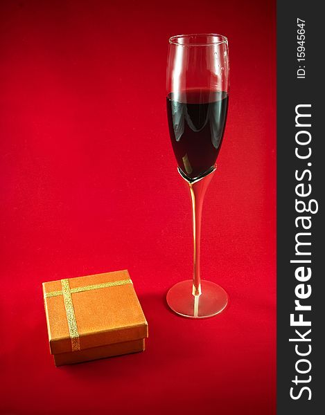 Elegant wineglass, red wine and gift box on red background. Elegant wineglass, red wine and gift box on red background