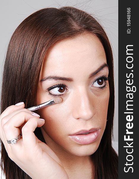 A young pretty girl put the last bit of makeup on her face, over light gray background. A young pretty girl put the last bit of makeup on her face, over light gray background.