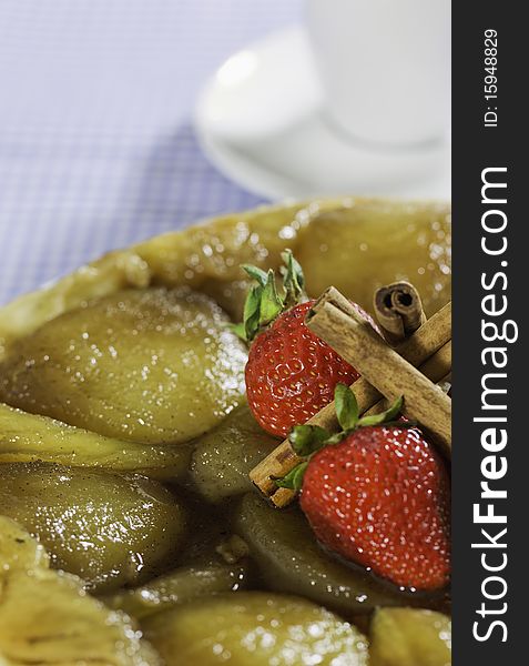 French style apple pie with stawberry and cinnamon on the top.Coffee cup in the background. Shallow depth of field.