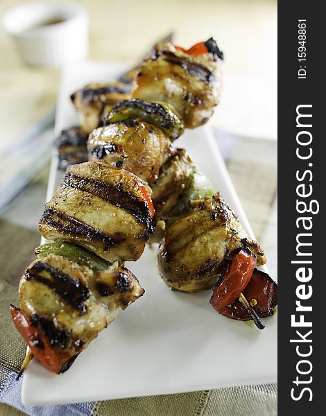 Grilled chicken skewers on a white plate with vegetables. Shallow depth of field.
