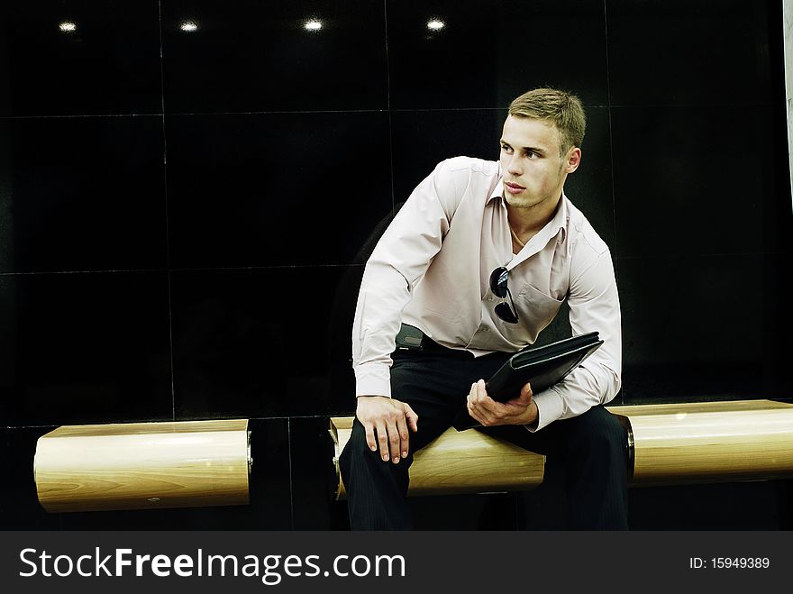 The attractive young man with a folder sits on a bench and expects a meeting. The attractive young man with a folder sits on a bench and expects a meeting.