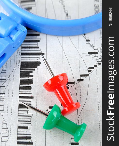 A blue magnifier and drawing pin in red and green color, putting on a stock graph, means business and finance analysis and key point. A blue magnifier and drawing pin in red and green color, putting on a stock graph, means business and finance analysis and key point.