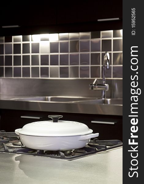 A simple arrangement of a white pot with lid on a gas stove and metallic background. A simple arrangement of a white pot with lid on a gas stove and metallic background