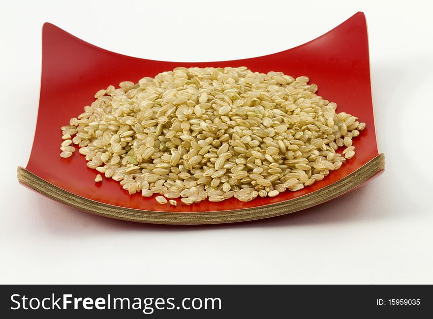 Raw, uncooked brown rice mounded on curved, red dish. Raw, uncooked brown rice mounded on curved, red dish