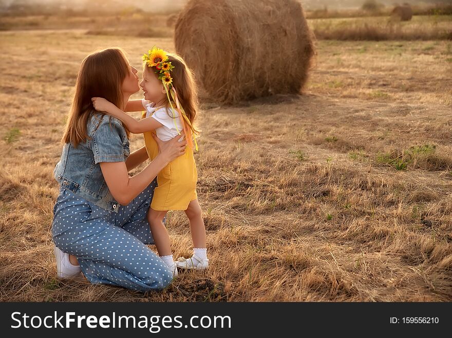 Happy girl child in yellow dress hugs young mom in autumn field