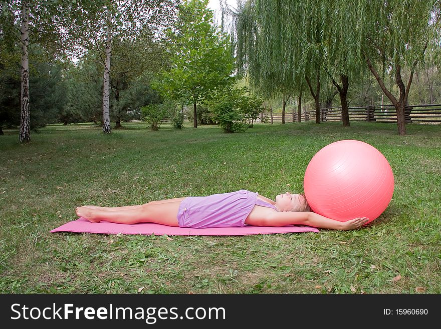 Girl engages in yoga, a large ball lies on a carpet and get on the hip