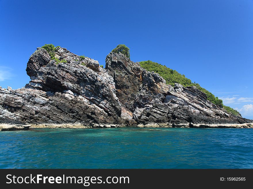 A rocky island with greens in the middle of the sea with blue skies on the background. Location - Perhentian Island, Terengganu, Malaysia. A rocky island with greens in the middle of the sea with blue skies on the background. Location - Perhentian Island, Terengganu, Malaysia