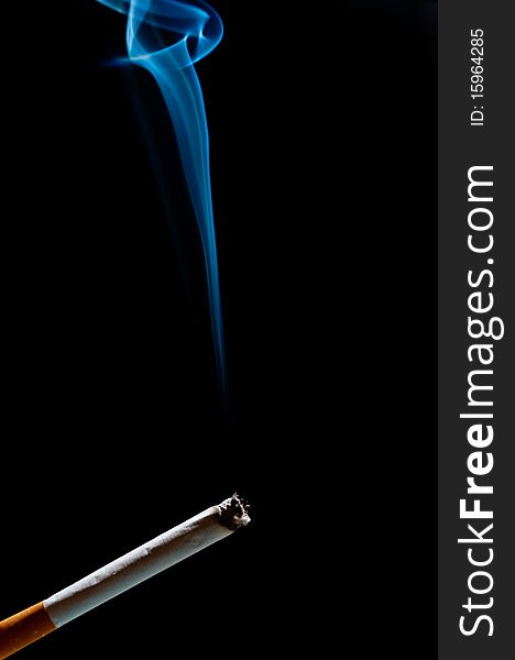 Cigarette in front of black background. smoke goes up. Cigarette in front of black background. smoke goes up