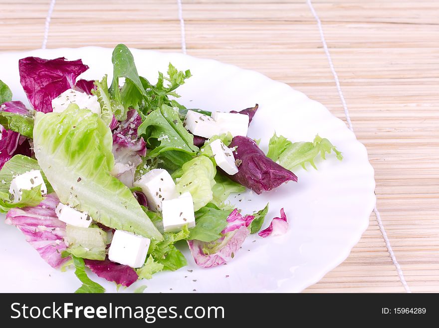 Leafs salad  with sheep cheese on plate,closed-up on wooden mat