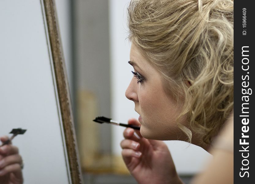 Horizontal image of a young woman applying makeup in a mirror