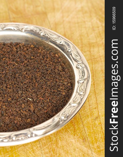 Loose black tea leaves in a sterling silver dish on a wooden surface. Loose black tea leaves in a sterling silver dish on a wooden surface