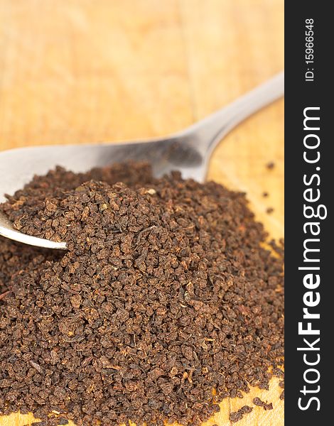 Loose black tea leaves spill from a spoon onto a wooden surface