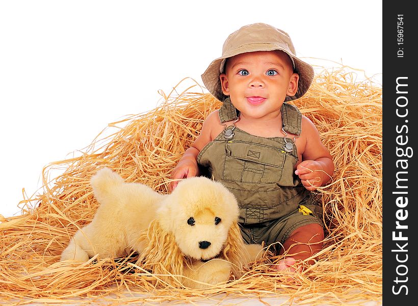 A happy, biracial baby boy in overalls playing in a pile of hay with his toy pup.  Isolated on white. A happy, biracial baby boy in overalls playing in a pile of hay with his toy pup.  Isolated on white.