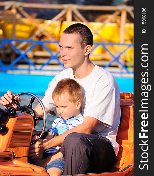 The father and the son go for a drive on the toy car. The father and the son go for a drive on the toy car