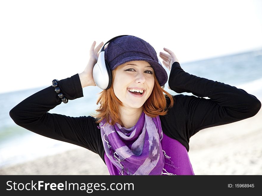 Red-haired girl in cap with headphone on the beach show OK symbol. Red-haired girl in cap with headphone on the beach show OK symbol.