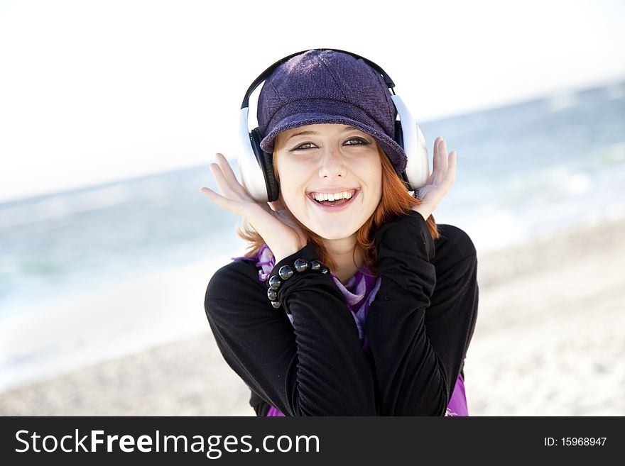 Red-haired girl in cap with headphone on the beach show OK symbol. Red-haired girl in cap with headphone on the beach show OK symbol.