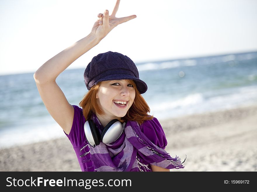 Red-haired girl in cap with headphone on the beach show OK symbol. Red-haired girl in cap with headphone on the beach show OK symbol.