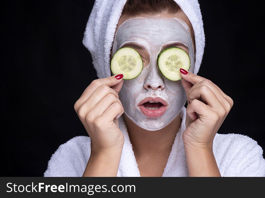 Beautiful young european woman apply clay mask on her face with towel on her head and cucumbers on her eyes. beauty spa concept
