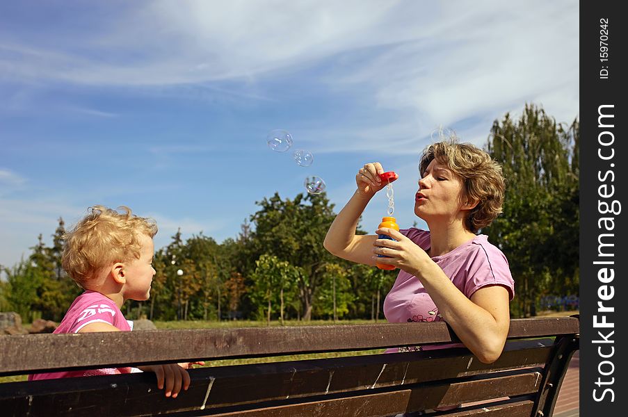 Mother and son blowing soap bubbles on the bench in a park