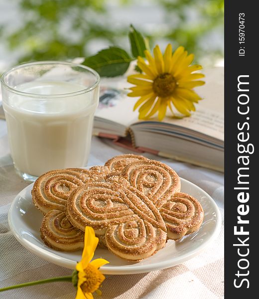 Glass of milk with two cookies. Book with flower on background. Glass of milk with two cookies. Book with flower on background