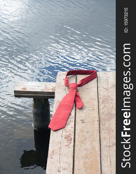 Concept with red necktie lying on wooden pier on background with river. Concept with red necktie lying on wooden pier on background with river