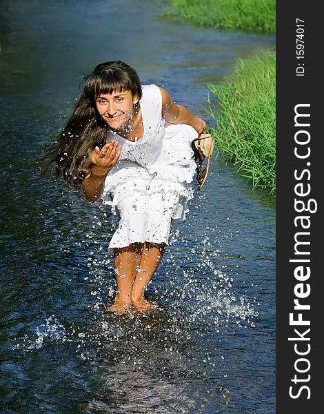 Young attractive  lady in white dress smiling and  splashing in the stream. Young attractive  lady in white dress smiling and  splashing in the stream