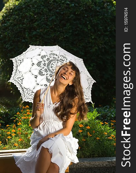 Happy attractive girl in white dress with sun umbrella sitting and laughing on the bench in the park. Happy attractive girl in white dress with sun umbrella sitting and laughing on the bench in the park