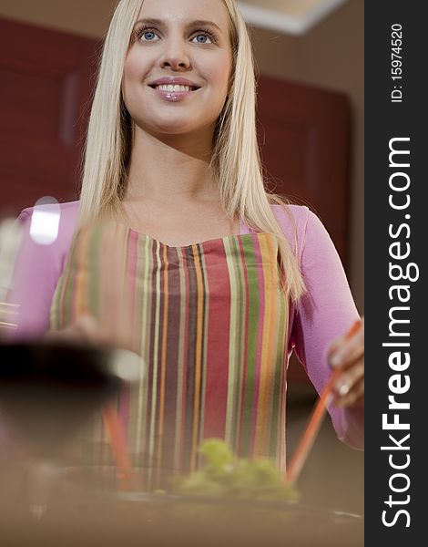 Young woman preparing salad, displaying a red glass of wine; selective focus. Young woman preparing salad, displaying a red glass of wine; selective focus