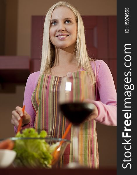 Young woman preparing salad, displaying a red glass of wine; selective focus. Young woman preparing salad, displaying a red glass of wine; selective focus