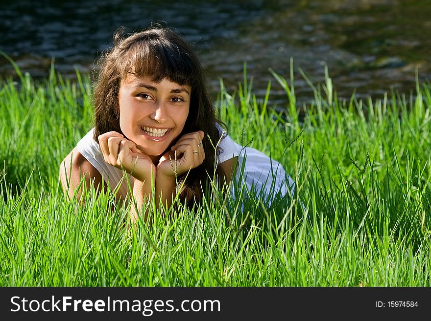 Young smiling girl liying on the fresh green grass near the river. Young smiling girl liying on the fresh green grass near the river