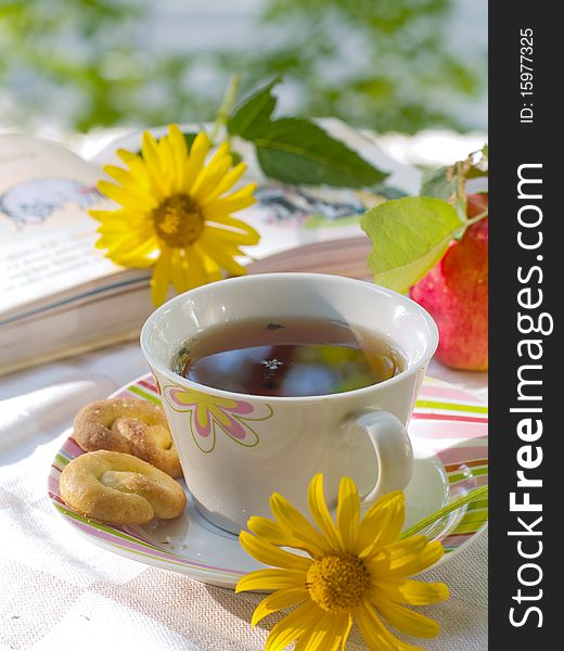 Tea with cookies, the book and flowers on background