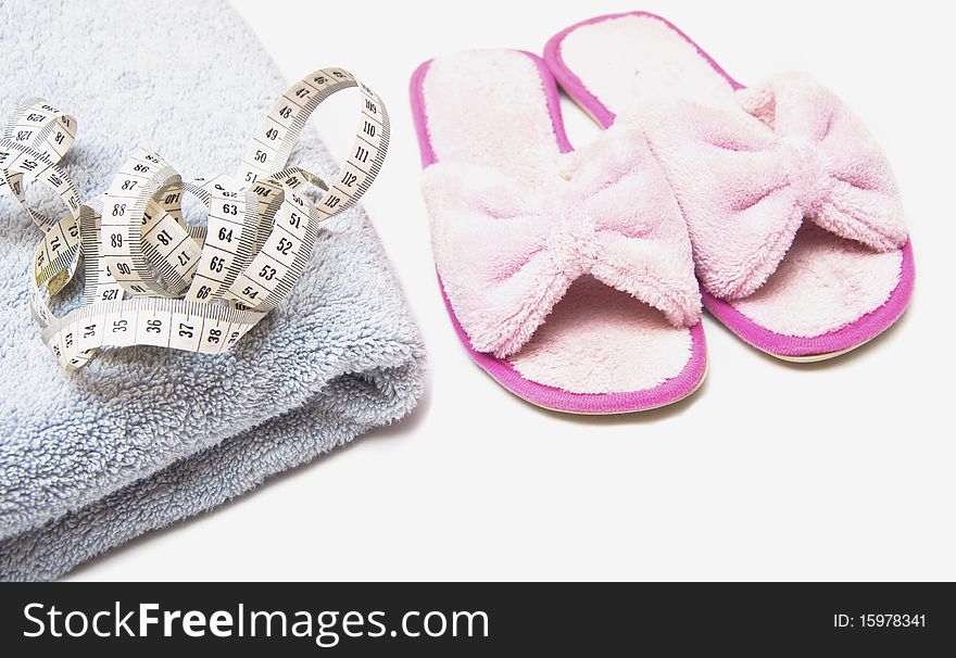 Slippers, grey folded towel and metr on white