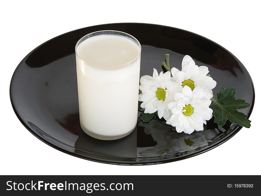 Glass of milk and white camomiles with reflection on a black dish