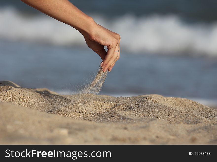 Female hand pours sand on the shore